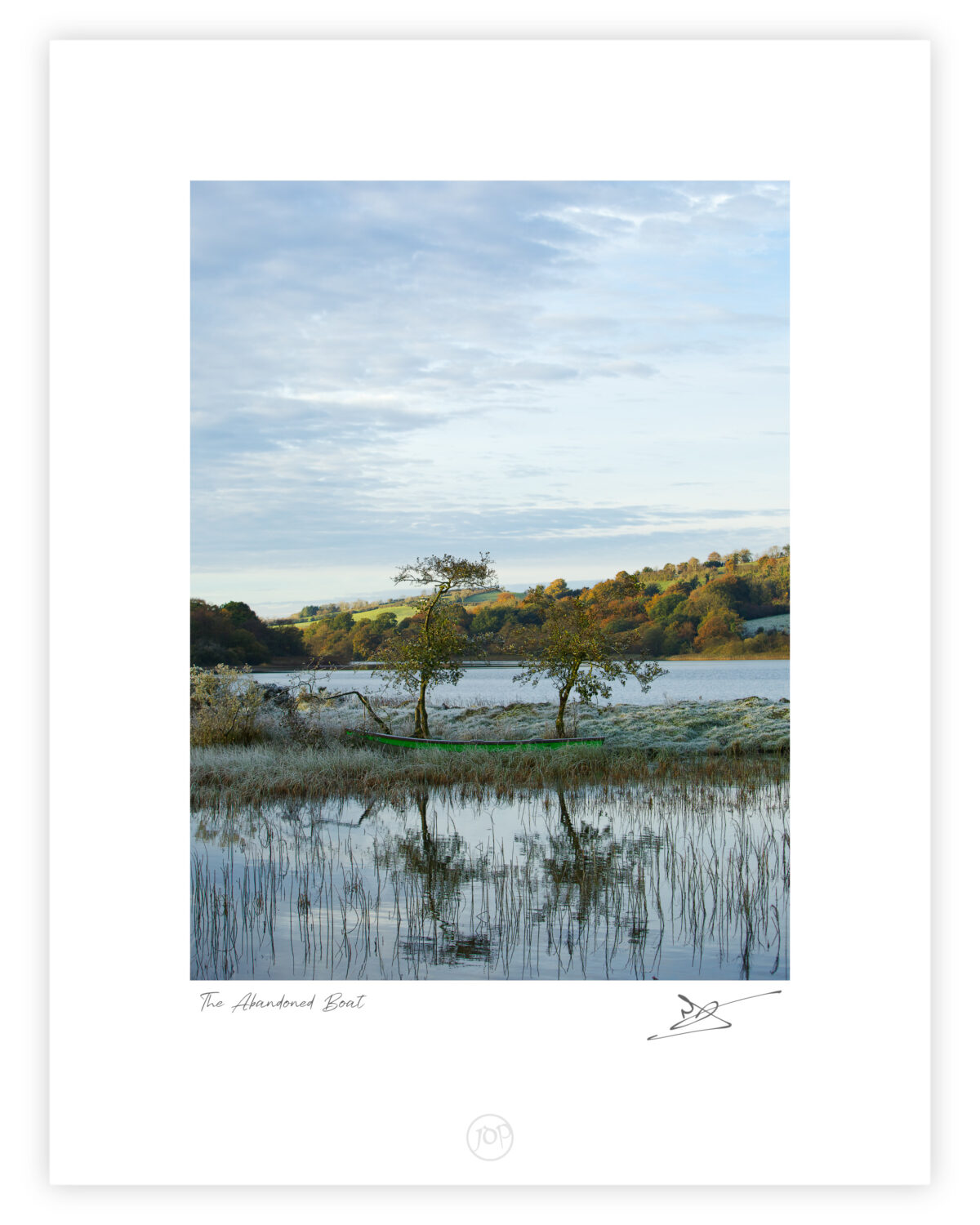Rowboat beside a still lake with two trees and autumn hills reflected in the water in County Cavan.