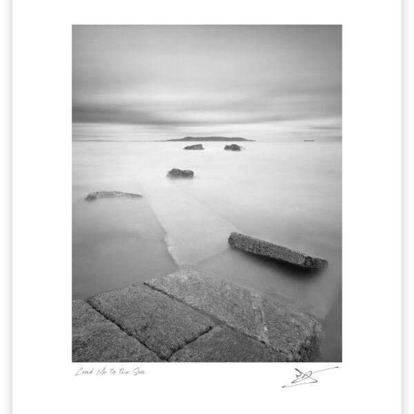 Black and white long exposure from Sandycove slipway looking across Dublin Bay toward Howth Head, with stone steps leading into calm water.