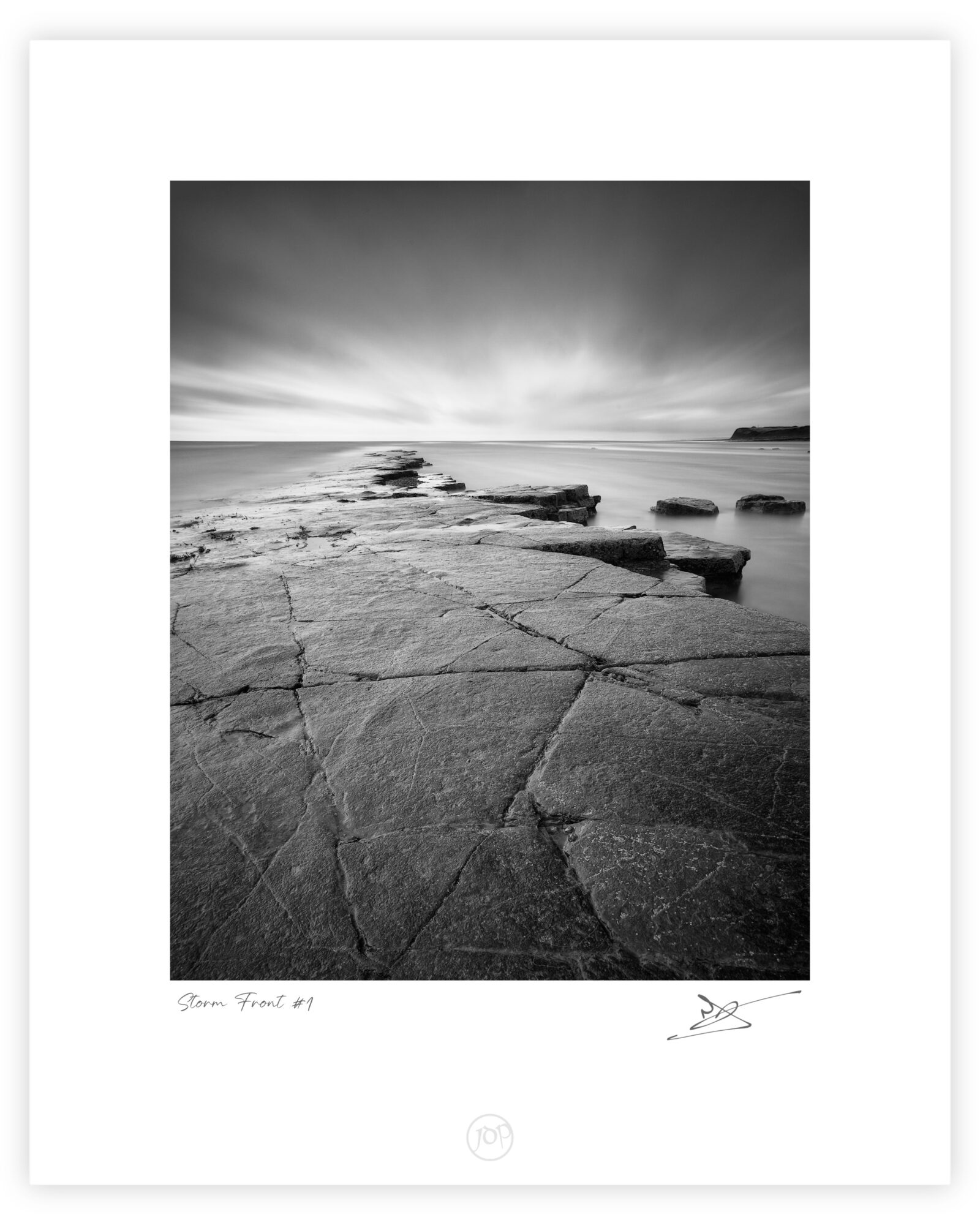 Rock shelf and calm sea beneath storm clouds at Kimmeridge Bay on the Dorset coast, black and white photograph.