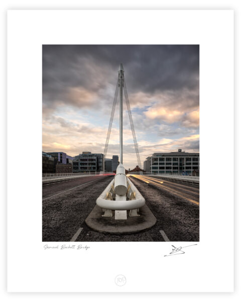 Samuel Beckett Bridge in Dublin seen head-on at dusk with long-exposure car light trails and dramatic clouds.