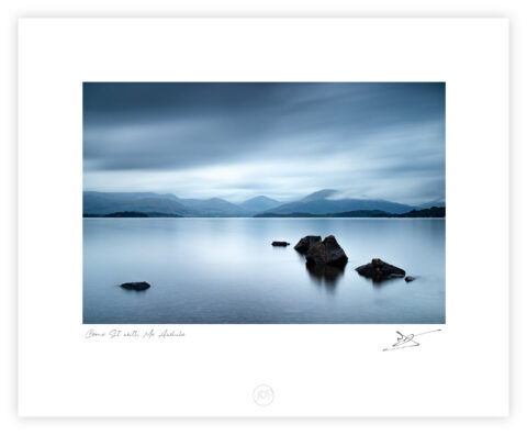Stones in calm water at Millarochy Bay on Loch Lomond with mountains and fast-moving clouds, Scotland, colour photograph.