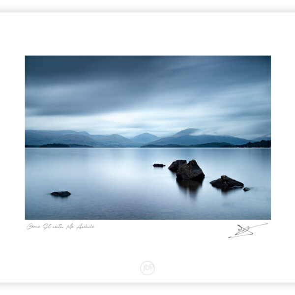 Stones in calm water at Millarochy Bay on Loch Lomond with mountains and fast-moving clouds, Scotland, colour photograph.