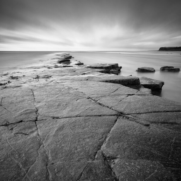Rock shelf and calm sea beneath storm clouds at Kimmeridge Bay on the Dorset coast, black and white photograph.