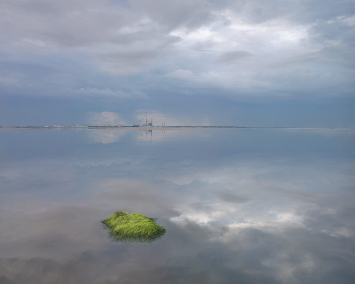 The Stillness after the Storm - Calm, Tranquil, Stillness Moss-covered rock reflected in still water at Blackrock, Dublin Bay, with Poolbeg chimneys on the horizon.