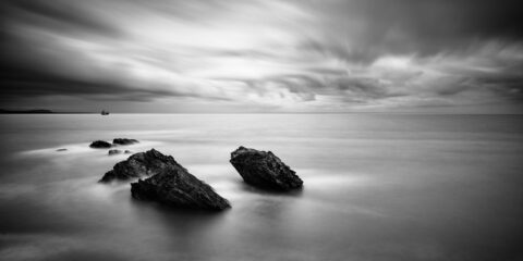 Cargo ship leaving Wicklow Port with rocks in the foreground and clouds over the Irish Sea.