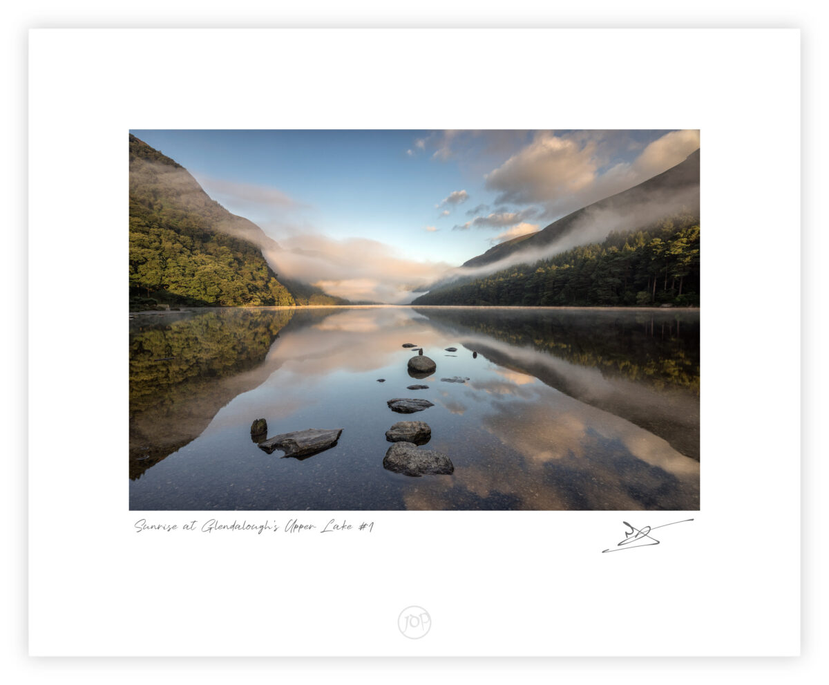 Mist rising over Upper Lake in Glendalough with rocks reflected in still water in County Wicklow.