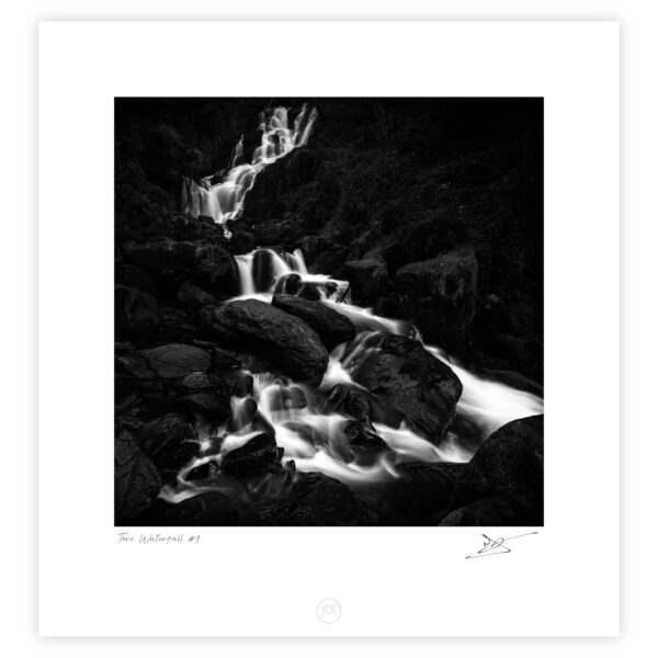 Black and white photograph of Torc Waterfall flowing over rocks in Killarney National Park, Ireland.