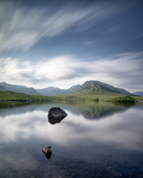 Mount Bencorr and the Twelve Pins reflected in calm water at Derryclare Lough in Connemara, Galway, Ireland, colour photograph.
