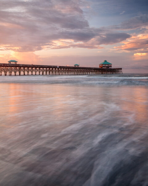 Folly Beach Fishing Pier at sunrise with soft waves and pastel sky in South Carolina, United States, colour photograph.