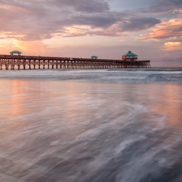 Folly Beach Fishing Pier at sunrise with soft waves and pastel sky in South Carolina, United States, colour photograph.