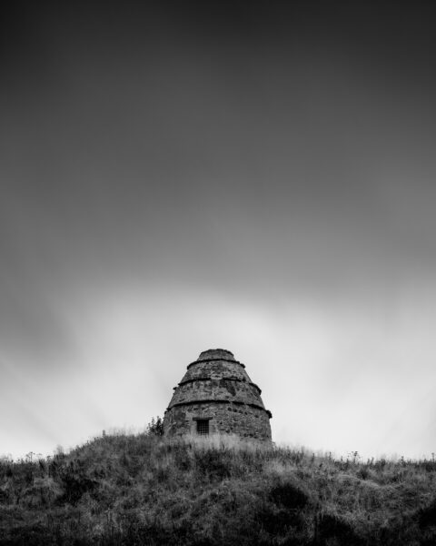 Stone dovecot of Dunure Castle on a grassy hill above the beach at Ayr, Scotland, black and white photograph.