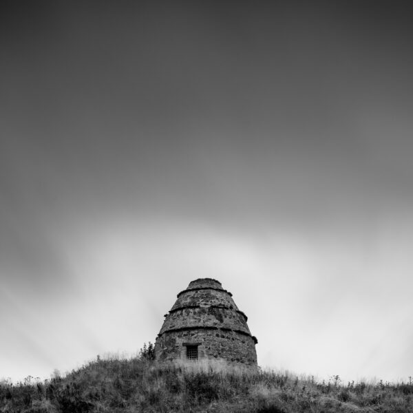 Stone dovecot of Dunure Castle on a grassy hill above the beach at Ayr, Scotland, black and white photograph.