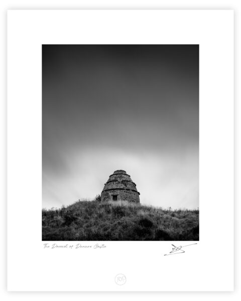 Stone dovecot of Dunure Castle on a grassy hill above the beach at Ayr, Scotland, black and white photograph.