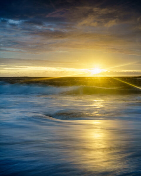 Sunset light breaking beneath clouds over the Atlantic at Murder Hole Beach on the Rosguill Peninsula in Donegal, Ireland, colour photograph.