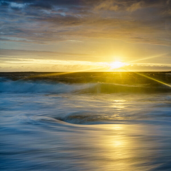 Sunset light breaking beneath clouds over the Atlantic at Murder Hole Beach on the Rosguill Peninsula in Donegal, Ireland, colour photograph.
