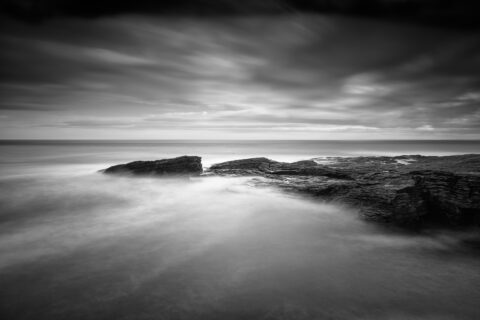 Black and white long-exposure photograph of waves flowing over layered rock shelves at Hook Head on the Wexford coast, Ireland.