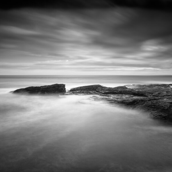 Black and white long-exposure photograph of waves flowing over layered rock shelves at Hook Head on the Wexford coast, Ireland.