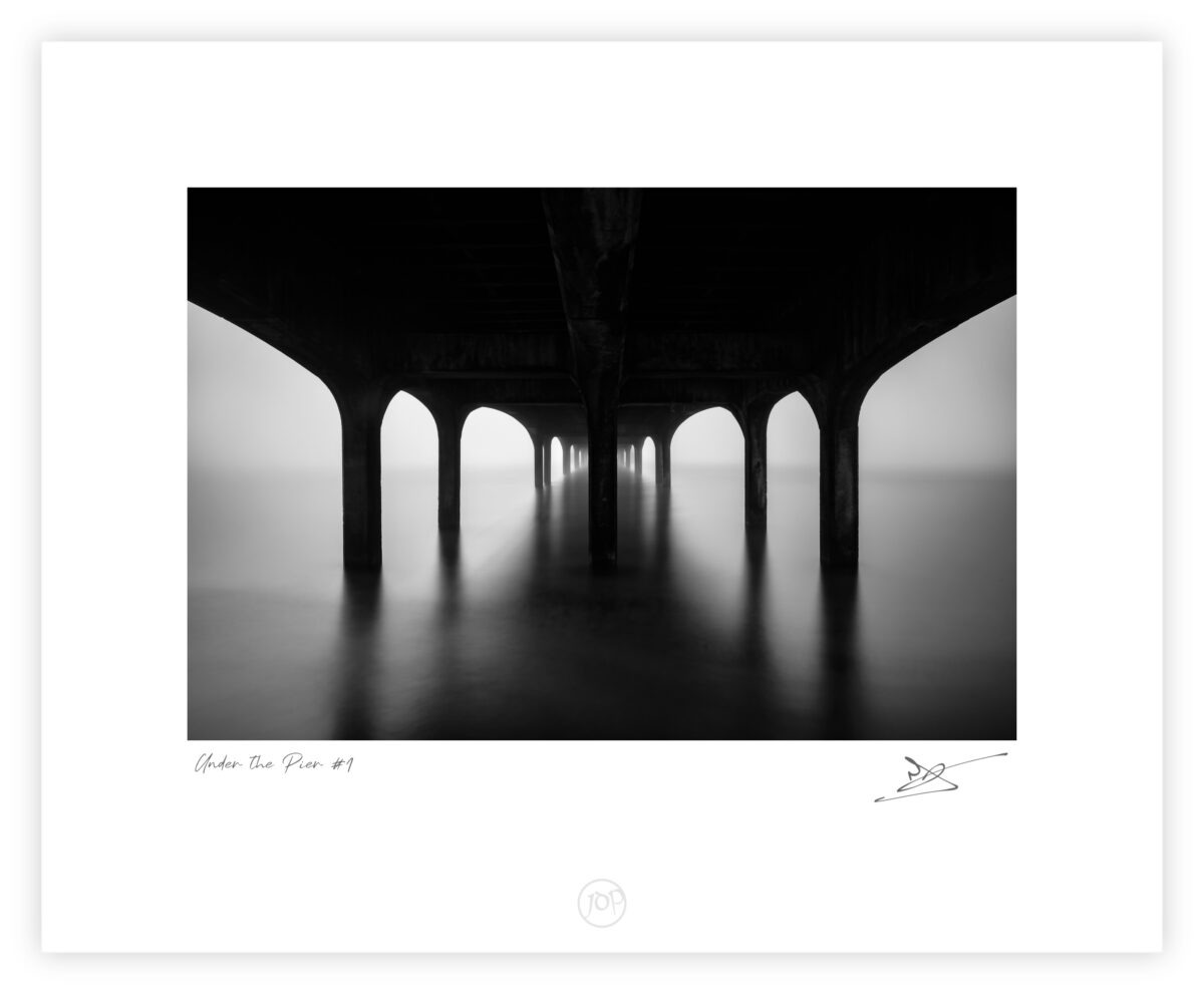 Under Boscombe Pier at dawn with still water and repeating arches in Bournemouth, England, black and white photograph.