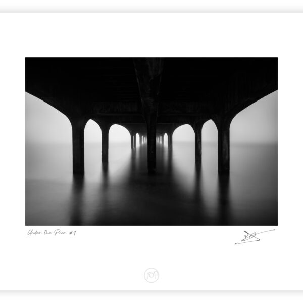 Under Boscombe Pier at dawn with still water and repeating arches in Bournemouth, England, black and white photograph.
