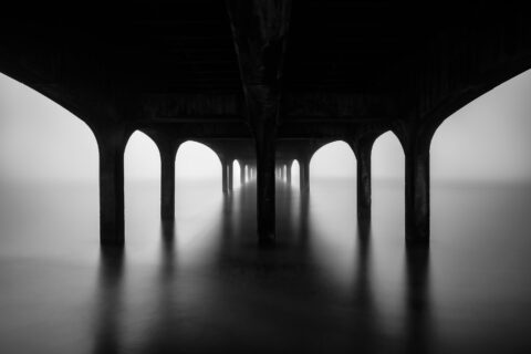 Under Boscombe Pier at dawn with still water and repeating arches in Bournemouth, England, black and white photograph.