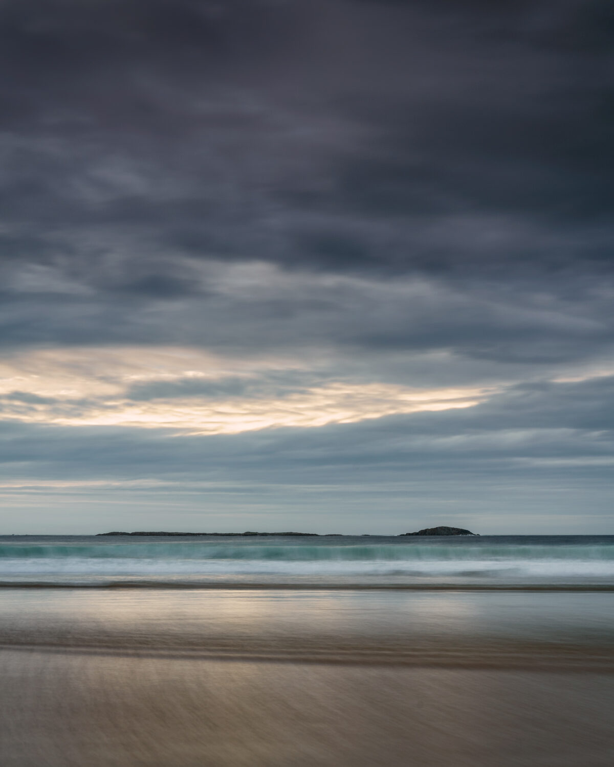 Sunset at Tramore Strand # 1 Tramore Strand near Downings in Donegal at sunset with soft waves, pastel sky, and distant islands, Ireland, colour photograph.