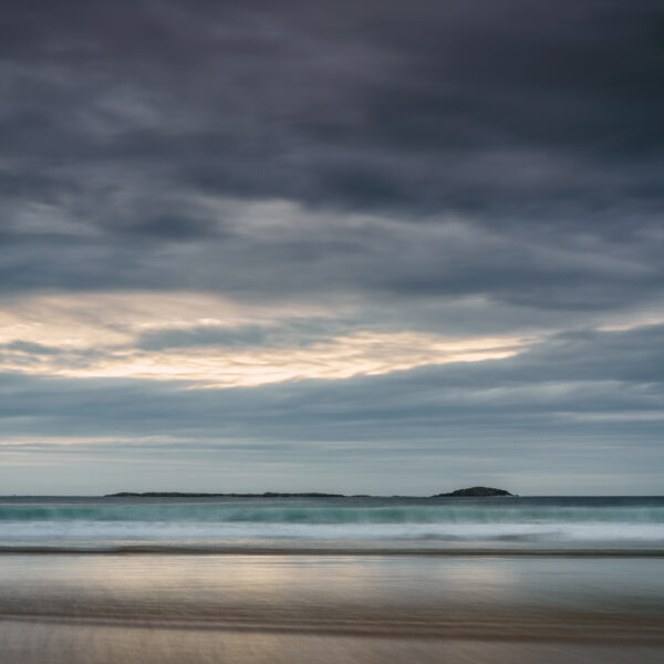 Tramore Strand near Downings in Donegal at sunset with soft waves, pastel sky, and distant islands, Ireland, colour photograph.