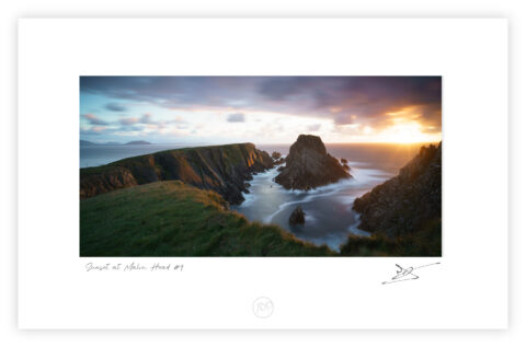 Cliffs and sea at Malin Head in Donegal lit by warm sunset light beneath dramatic clouds, Ireland, colour photograph.