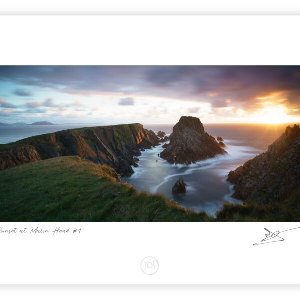 Cliffs and sea at Malin Head in Donegal lit by warm sunset light beneath dramatic clouds, Ireland, colour photograph.