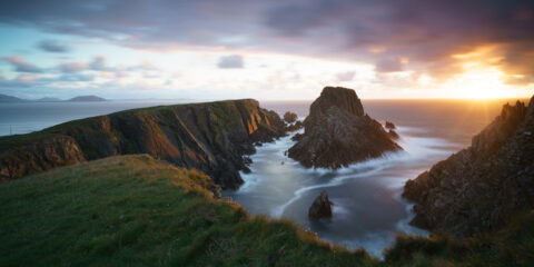 Cliffs and sea at Malin Head in Donegal lit by warm sunset light beneath dramatic clouds, Ireland, colour photograph.