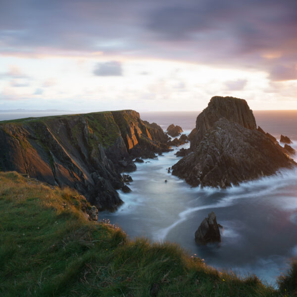 Cliffs and sea at Malin Head in Donegal lit by warm sunset light beneath dramatic clouds, Ireland, colour photograph.