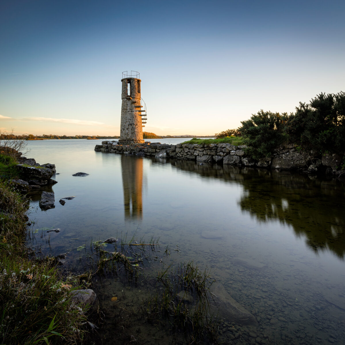 Sunset at Ballycurrin Lighthouse #2 - Sunset. Quiet, Calm Ballycurrin Lighthouse reflected in calm water on Lough Corrib at sunset in Galway, Ireland, colour photograph.