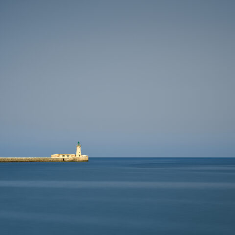 St Elmo Lighthouse on the breakwater viewed from Valletta with calm sea and clear sky, Malta, colour photograph.