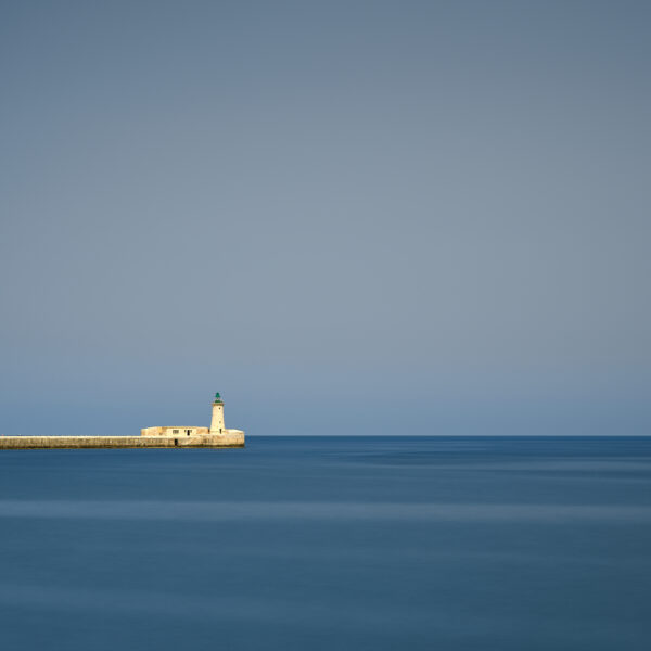 St Elmo Lighthouse on the breakwater viewed from Valletta with calm sea and clear sky, Malta, colour photograph.