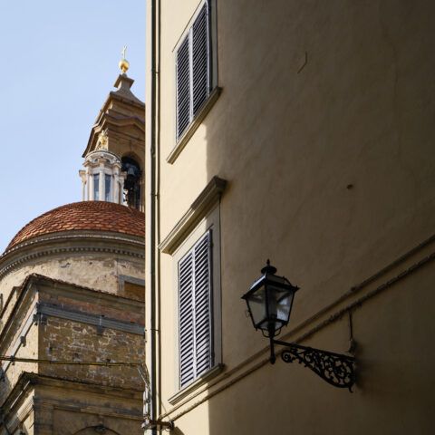 Sunlit Florentine street with sharp shadows framing the steeple of the Basilica di San Lorenzo, Florence, Italy, colour photograph.