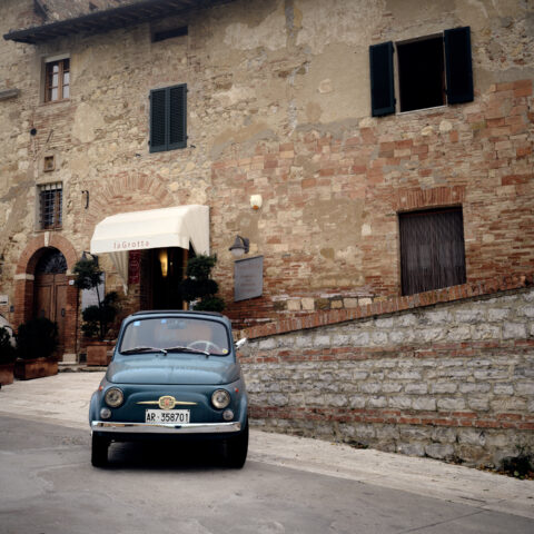 Vintage Fiat 500 parked beside stone buildings near San Biagio in Montepulciano, Italy, colour photograph.