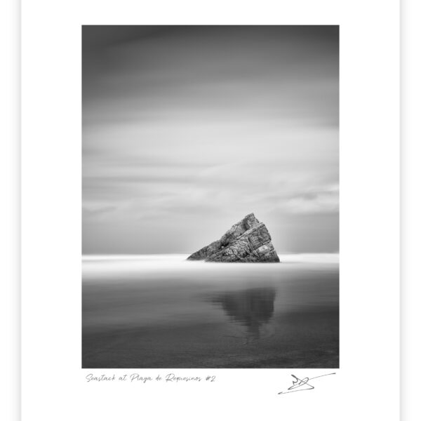 Black and white long exposure photograph of a leaning sea stack rising from calm reflective water at Playa de Requesinos, Asturias, Spain.