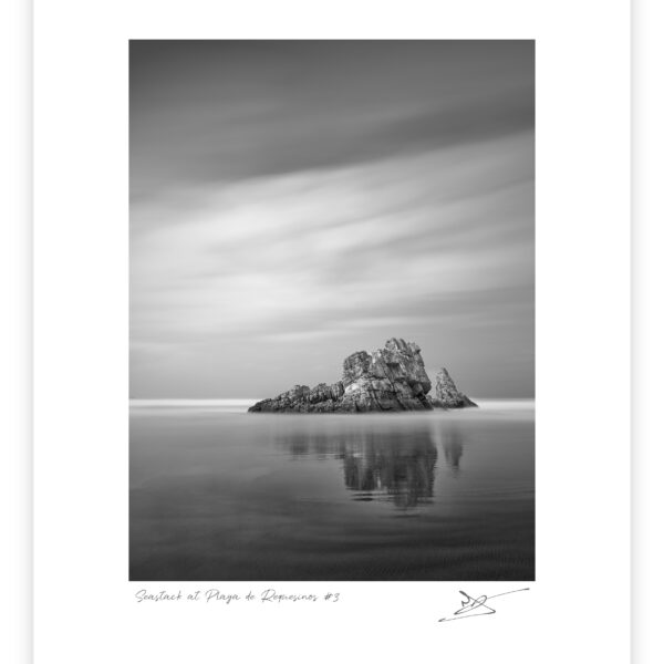 Black and white long exposure photograph of a low, jagged sea stack emerging from smooth tidal water with a soft sky above, Playa de Requesinos, Asturias, Spain.