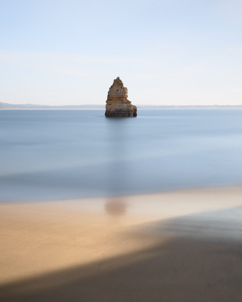 Sea stack rising from calm water off Praia do Camilo beach in the Algarve, Portugal.
