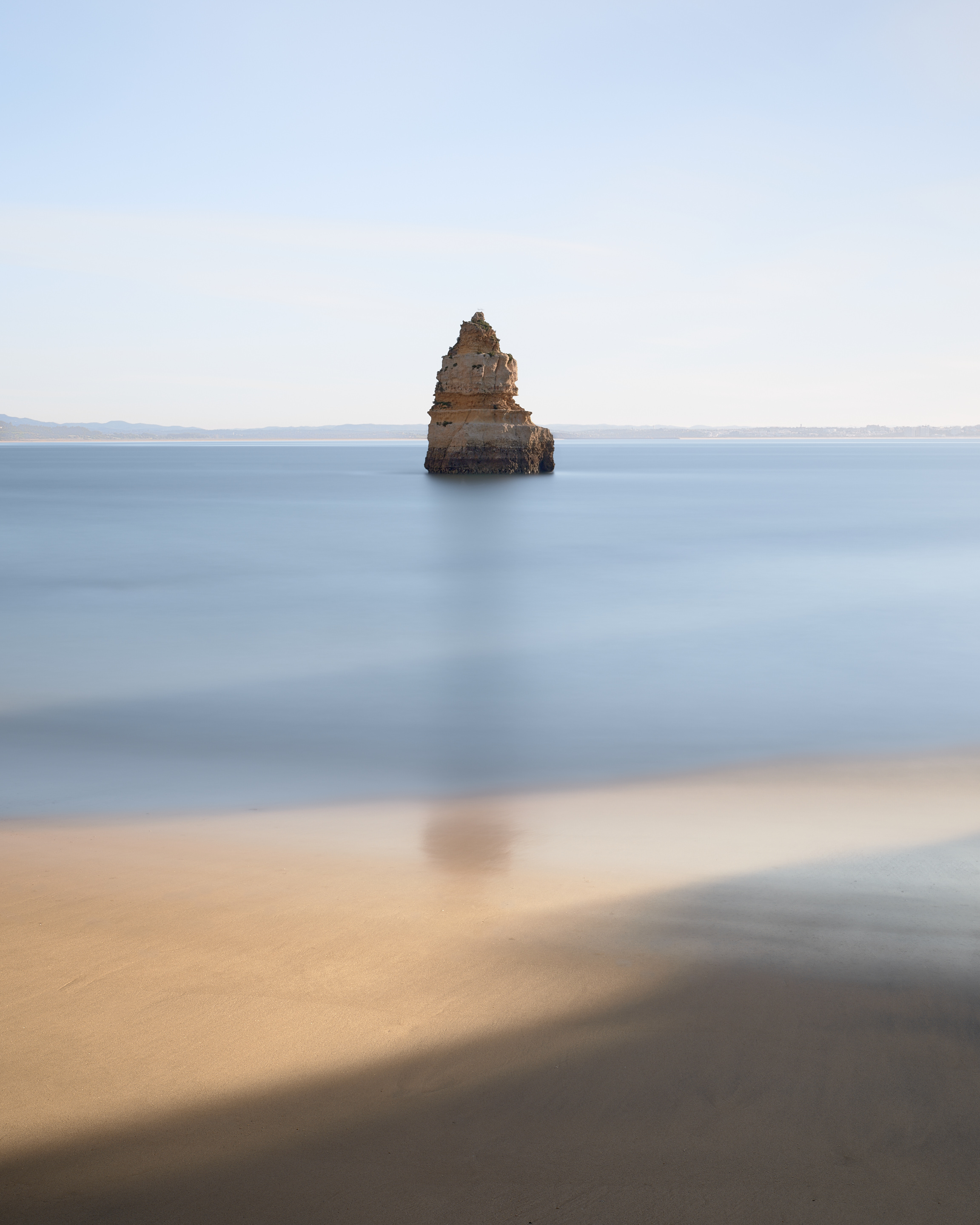 Sea stack rising from calm water off Praia do Camilo beach in the Algarve, Portugal.