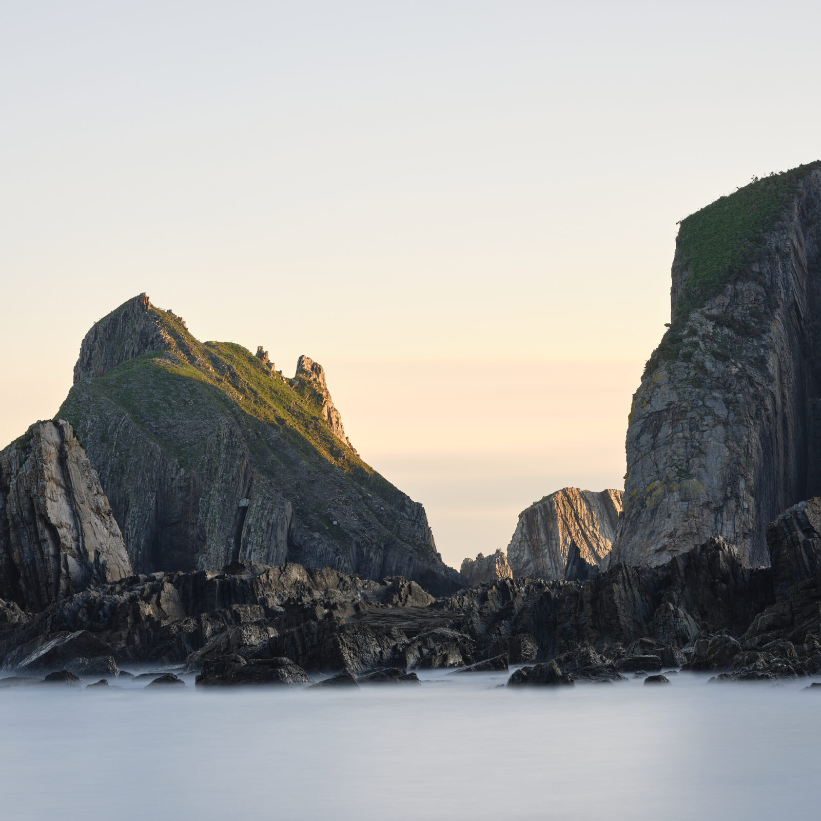 Towering cliff faces framing a smooth, long exposure tide at Playa del Silencio in Asturias, Spain, colour photograph.
