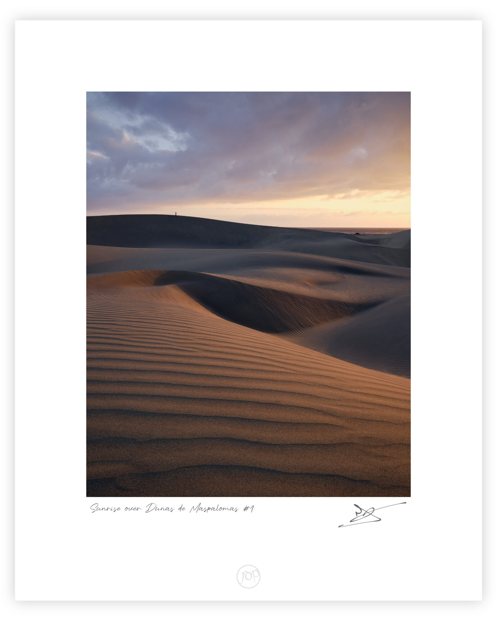Layered sand dunes at Maspalomas curve across the foreground and middle distance, their rippled surfaces lit by warm sunrise light beneath heavy blue-grey clouds, with a lone person standing on the far ridge and a narrow strip of sea beyond.