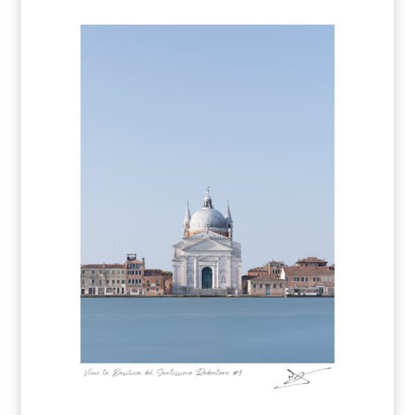 Centered view across smooth blue water to the white Basilica del Santissimo Redentore in Venice, framed by low terracotta-roofed buildings beneath a vast cloudless sky.
